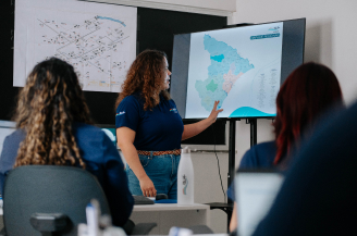 Profissional apresenta o mapa de obras do Portal de Obras de Infraestrutura em uma tela para participantes durante uma reunião.